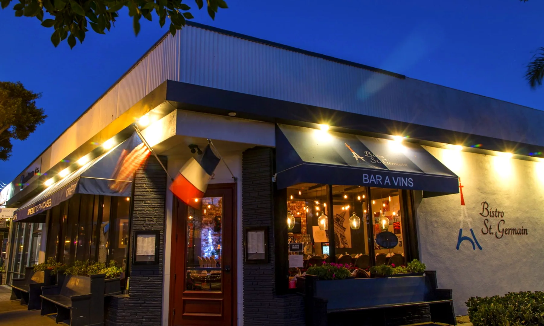 Exterior of Bistro St. Germain at dusk, French and American flags above the lit corner dining room
